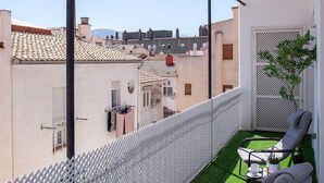 Un balcone con erba sintetica, due sedie, un recinto bianco e vista sugli edifici.