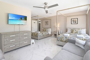 Ein Schlafzimmer mit Bett, Fernseher, Deckenventilator, Kommode und Spiegel im Badezimmer.