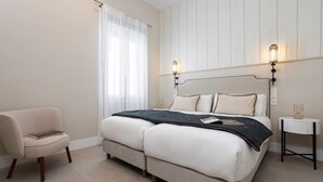 Ein Schlafzimmer mit einem Bett, Nachttischen, einem Sessel und einem Fenster mit Vorhängen.