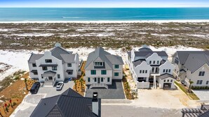 A coastal residential area with multiple houses, a paved driveway, and a clear view of the ocean. - Saylor's Delight: Beachfront NEW BUILD, Sugar Sands Mexico Beach, Private Pool & (Mexico Beach)