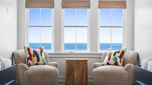 A room with three windows, a small wooden table, two armchairs, and a view of the ocean. - Saylor's Delight: Beachfront NEW BUILD, Sugar Sands Mexico Beach, Private Pool & (Mexico Beach)