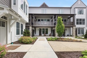 A two-story building with a front porch, stone pillars, and a small tree. - Gorgeous Union Pier Condo With Association Pool! Close To Beach and Downtown! (Union Pier)