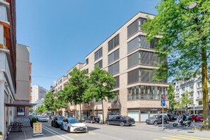 A multi-story building with a modern architectural style, featuring a mix of glass and brick facades, and a street with parked cars and trees. - CITY STAY - Franklinstrasse (Zürich)