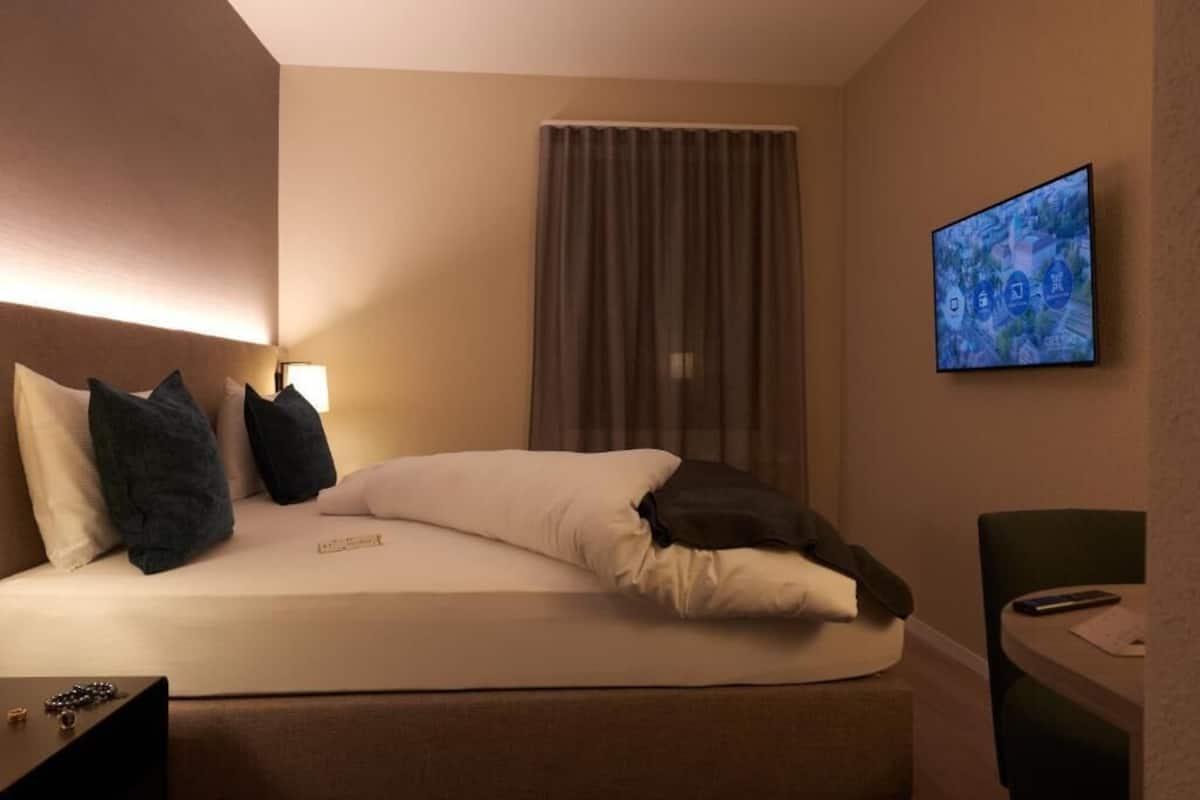 Habitación de hotel con cama, televisión montada en la pared, escritorio y silla.