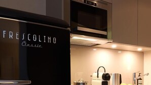 Una cocina con un refrigerador negro, un microondas, una tetera y un lavamanos.