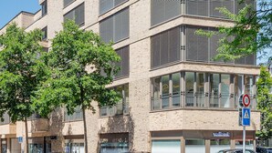 Un edificio de varios pisos con un diseño arquitectónico moderno, que combina ladrillo y elementos metálicos, ventanas amplias y una entrada visible.