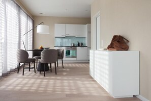 A modern kitchen with white cabinets, a dining area with a table and chairs, and a large window with sheer curtains. - CITY STAY - Franklinstrasse (Zürich)