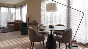 Una habitación de hotel moderna con una mesa redonda de comedor, cuatro sillas, un sofá, una mesa baja y una lámpara.