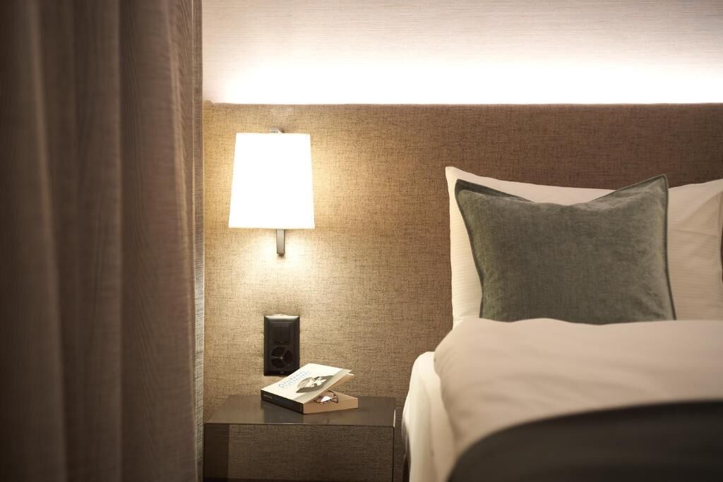 Une chambre d’hôtel avec un lit bien fait, une table de chevet avec une lampe et un téléphone fixé au mur.