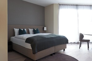 A modern hotel room with a large bed, a bedside table, a chair, and a view of the outdoors through a window. - CITY STAY - Franklinstrasse (Zürich)