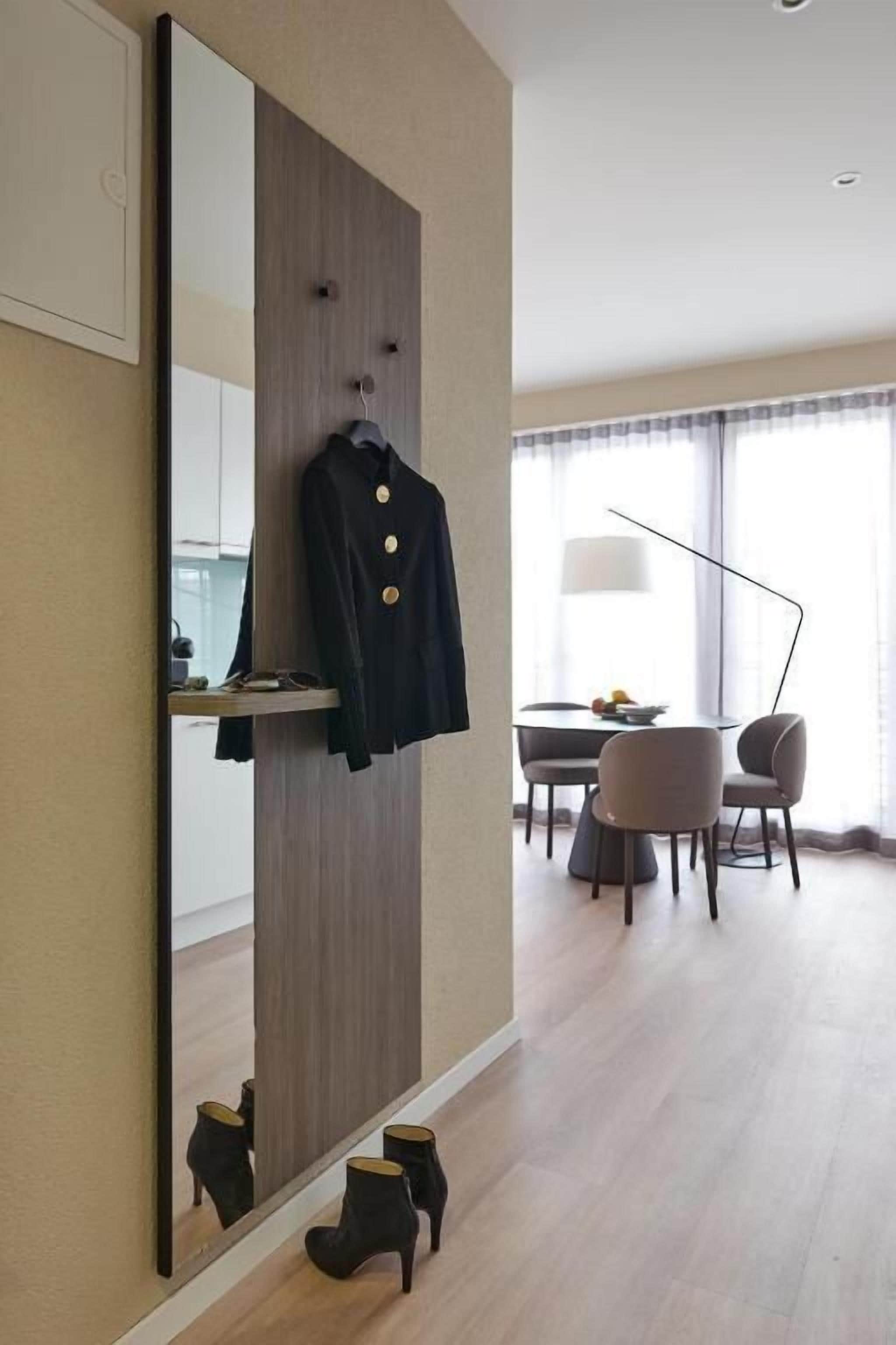Une chambre d’hôtel dotée d’un grand miroir, d’un porte-manteau, d’un coin repas avec une table et des chaises, et d’une lampe.
