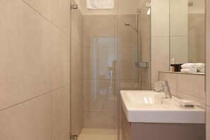 Un baño moderno con cabina de ducha de vidrio, lavabo blanco y espejo.