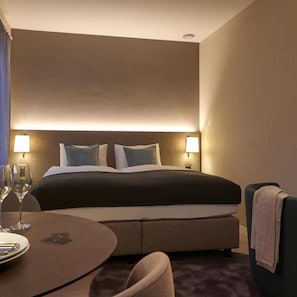 A hotel room with a bed, bedside lamps, a round table with a chair, and a small table with a wine glass and plate. - CITY STAY - Franklinstrasse (Zürich)