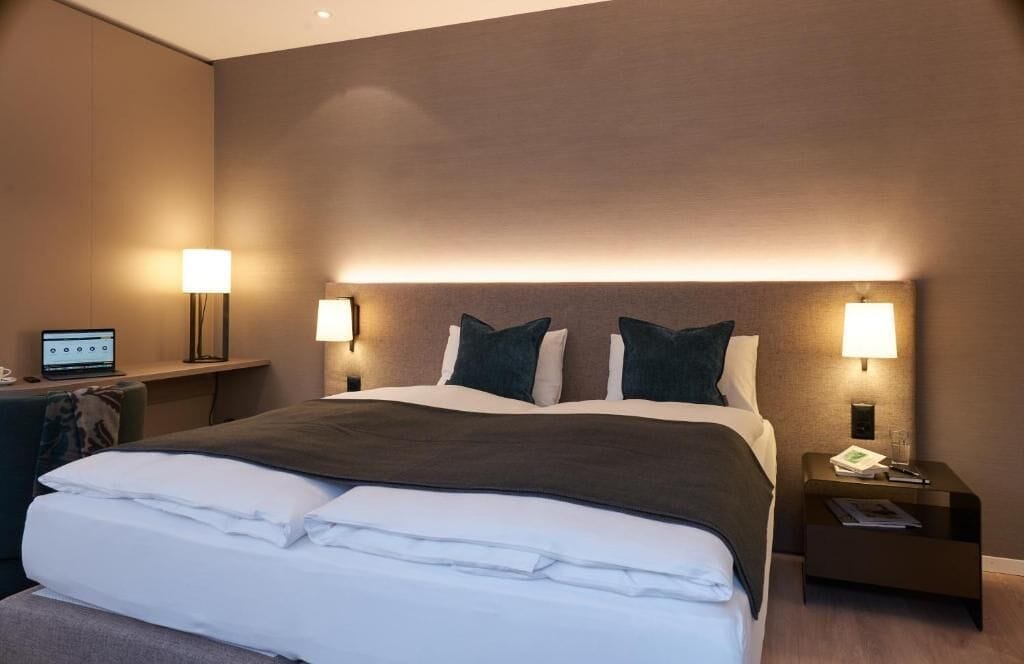 Une chambre d’hôtel avec un grand lit, deux tables de chevet avec des lampes, un bureau avec un ordinateur et un téléphone fixé au mur.