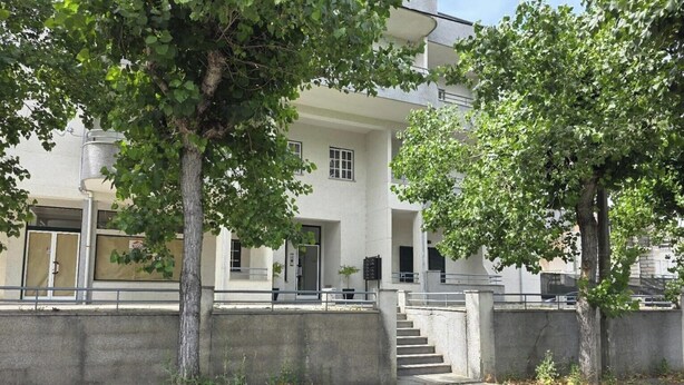 Ein modernes Gebäude mit flacher Fassade, großen Fenstern und einer Beton-Treppe, die zum Eingang führt.