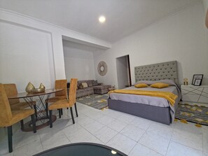 Ein Schlafzimmer mit einem Bett, einem Sofa, einem Esstisch mit Stühlen und einem kleinen Tisch mit Dekoration.