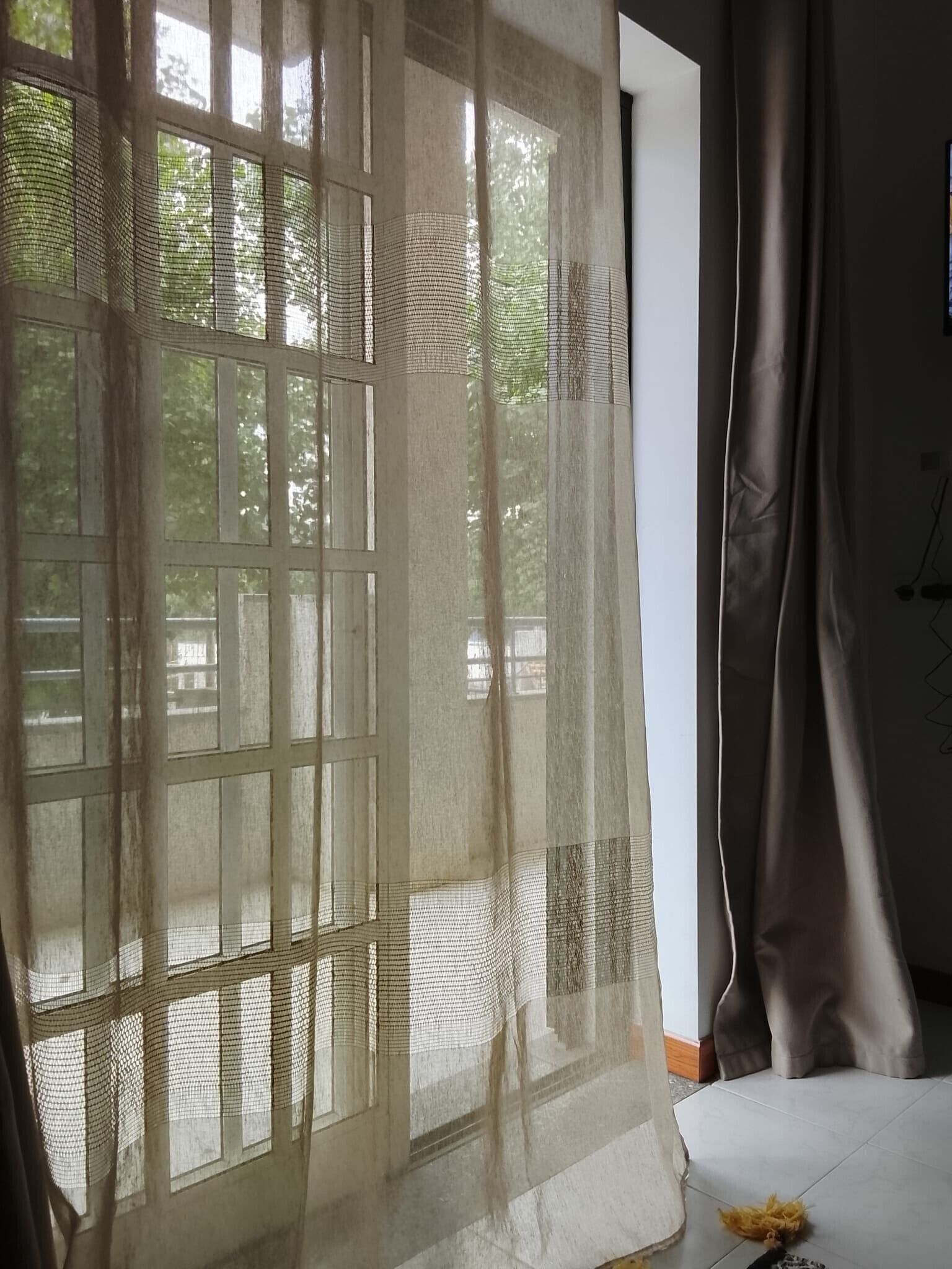 A room with a large window covered by sheer curtains, a bed, and a visible outdoor view.