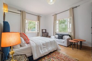 Une chambre à coucher avec un lit, un canapé, deux petites tables, une lampe et une fenêtre avec des rideaux.