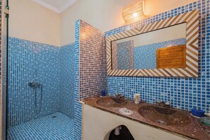 Une salle de bain avec des carreaux de mosaïque bleus, une douche, un lavabo avec un miroir et un porte-serviettes.