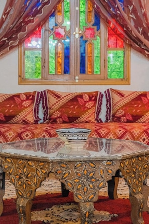 Una habitación con un sofá estampado, una mesita decorativa y una ventana de vitral.