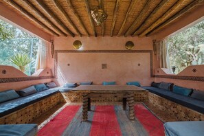 Una habitación con una gran mesa de madera, asientos acolchados, un papel tapiz estampado y un techo de paja.