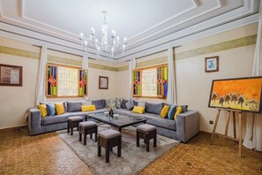 Ein geräumiges Zimmer mit einem großen grauen Sofa, einem Glastisch und einem Gemälde an der Wand.