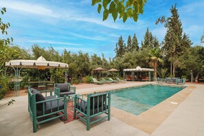 Zona junto a la piscina con sillones de descanso, un área de estar cubierta y vistas a árboles y vegetación.