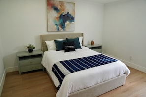A bedroom with a bed, nightstands, a wall art piece, and a small plant.