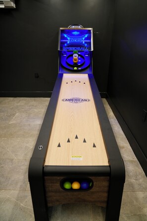A shuffleboard table with a digital score display, a wooden playing surface, and a caution label.