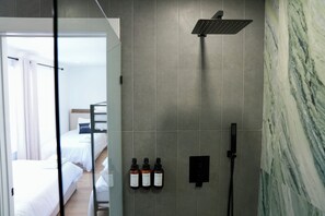 Et moderne badeværelse med bruser, tre shampoo flasker og en marmorvæg.
