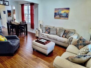 Una sala de estar con sofá, reposapiés y una mesa de comedor con sillas.