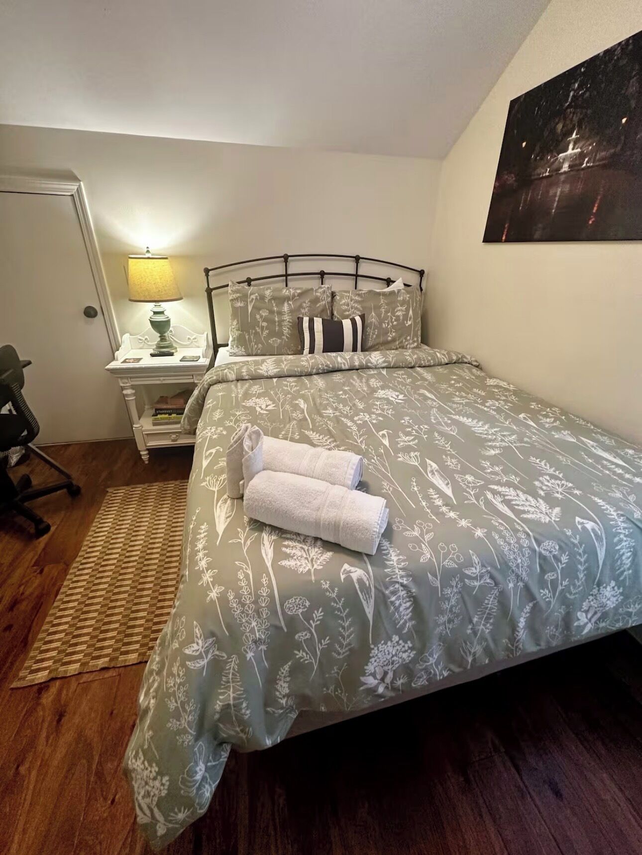 A neatly made bed with floral bedding, a bedside table with a lamp, and a chair.