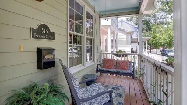 Varanda com uma placa indicando '315 Park Ave Cottage', área de estar com cadeiras estampadas e uma pequena mesa.