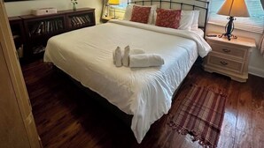 Cama bem arrumada com toalhas, ventilador de teto, um quadro, abajur e janela com cortinas.