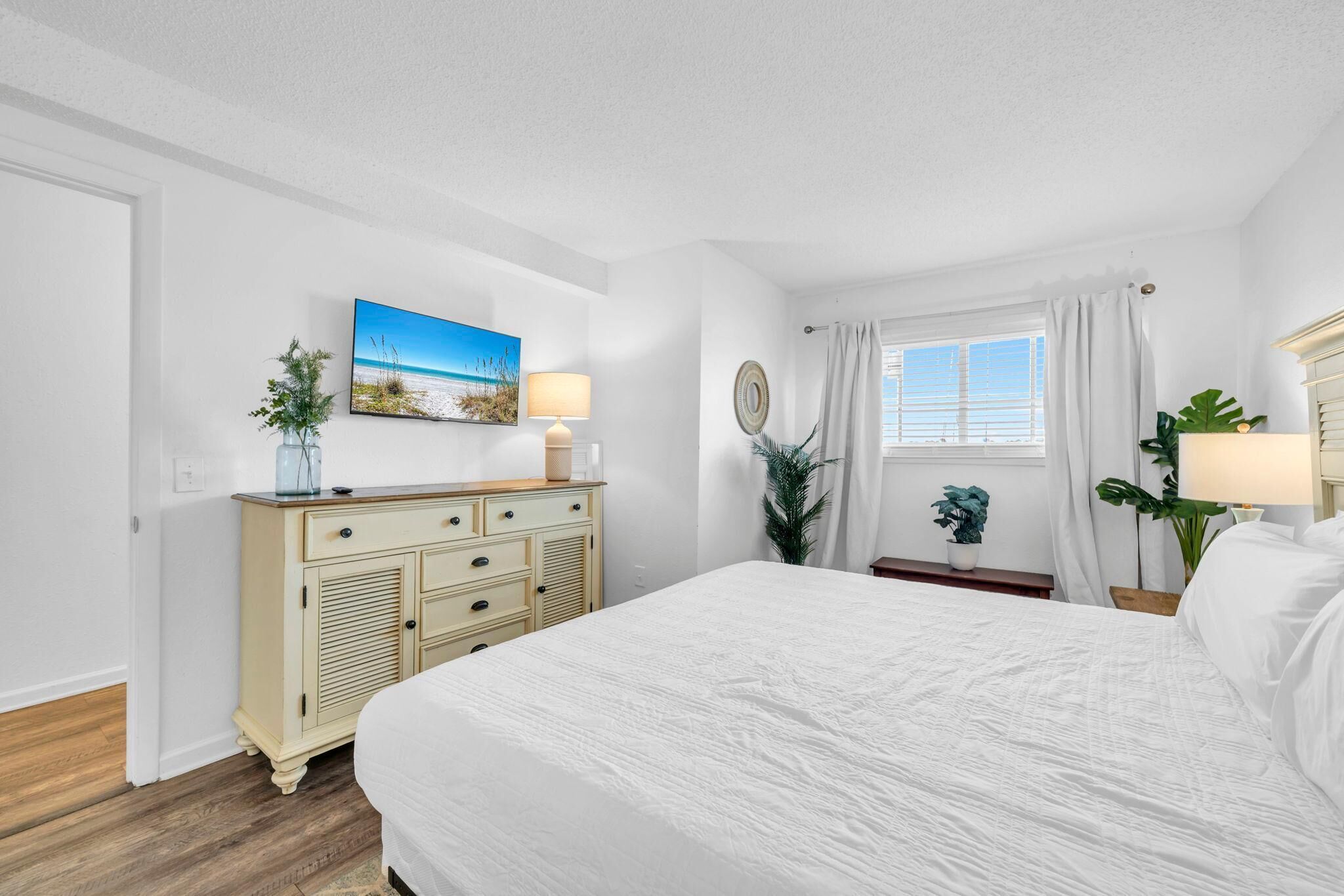 Un dormitorio con cama, cómoda, ventana con cortinas y un cuadro colgado en la pared.