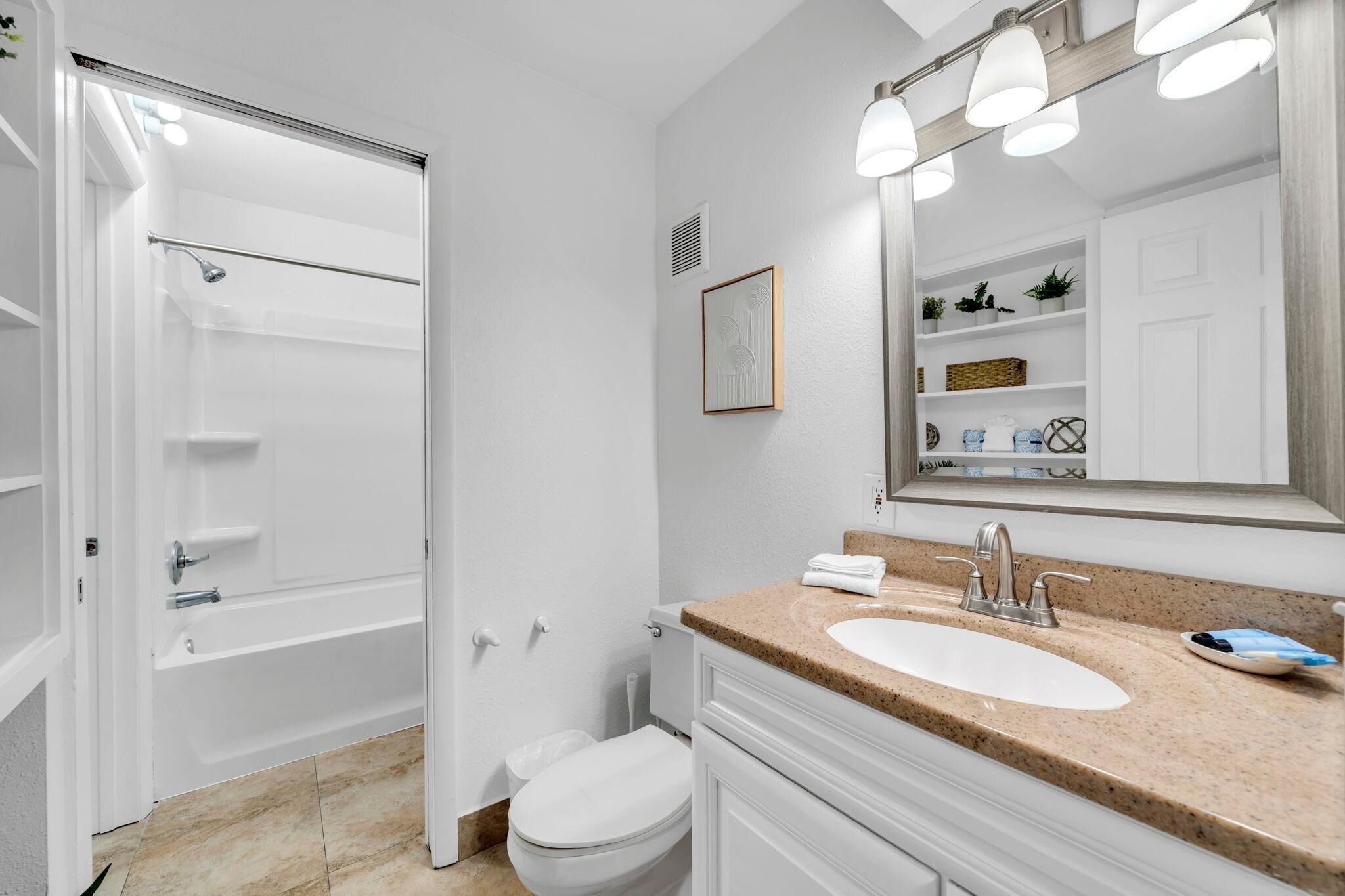 A bathroom with a shower, toilet, sink, and a large mirror.