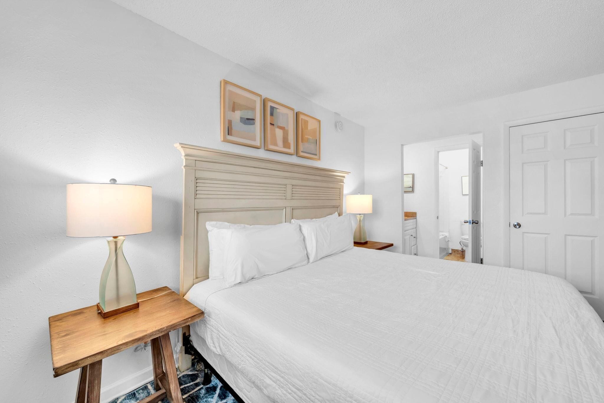 Une chambre d’hôtel avec un grand lit, deux tables de chevet avec des lampes, une tête de lit en bois et des tableaux encadrés au mur.