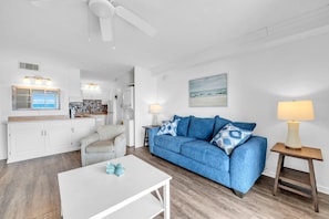 A modern living room with a blue sofa, white coffee table, and a kitchen area in the background. - The Summit 525 (Panama City Beach)