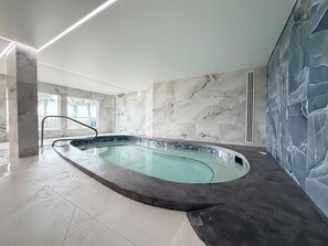 A modern indoor swimming pool with a marble wall and ceiling, a clear glass barrier, and a tiled floor. - The Summit 525 (Panama City Beach)