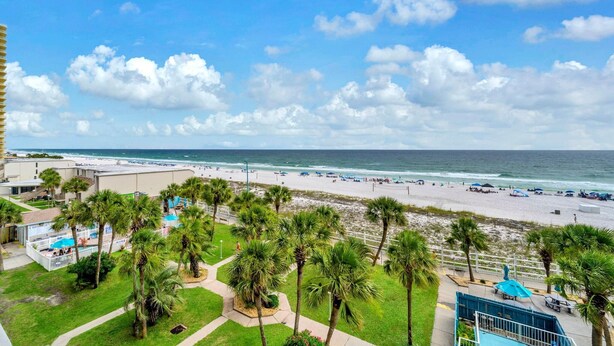 A beach view with palm trees, a pool, and a building with a balcony overlooking the ocean. - The Summit 525 (Panama City Beach)