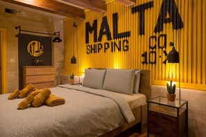 Ein Hotelzimmer mit einem Bett, einem Nachttisch, einer Lampe, einem an der Wand befestigten Schild und einer kleinen Topfpflanze.