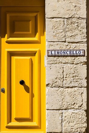 Eine gelbe Tür mit schwarzem Griff und einem Schild, auf dem 'LIMONCELLO' steht, an einer strukturierten Wand.