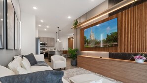Un salon moderne avec un grand téléviseur à écran plat fixé à un mur en bois, un canapé avec des coussins, une table basse et une plante en pot.