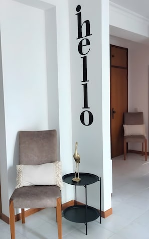 Ein modernes Zimmer mit einem grau gepolsterten Sessel, einem kleinen schwarzen Tisch mit einer goldfarbenen Vogel-Skulptur und einer Wand mit einem großen 'hello'-Schild.