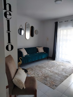Ein Wohnzimmer mit einem türkisfarbenen Sofa, einem runden Spiegel und einem Schild mit der Aufschrift 'hello'.