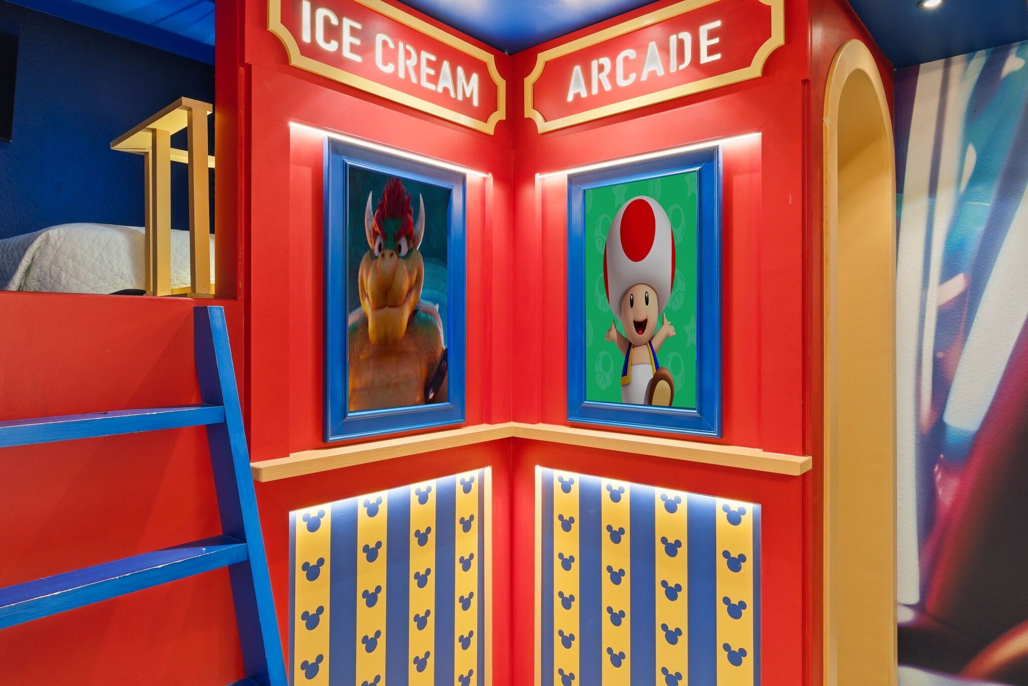 Une pièce avec un lit, une échelle et un mur orné d’enseignes de jeux d’arcade et de glaciers.