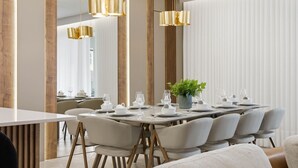 Ein moderner Essbereich mit einem langen Tisch, gedeckt für sechs Personen, umgeben von Stühlen, mit Pendelleuchten darüber.
