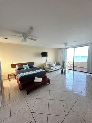 A hotel room with a bed, a sofa, a TV, and a view of the ocean. - Beachfront apartment (Cancún)