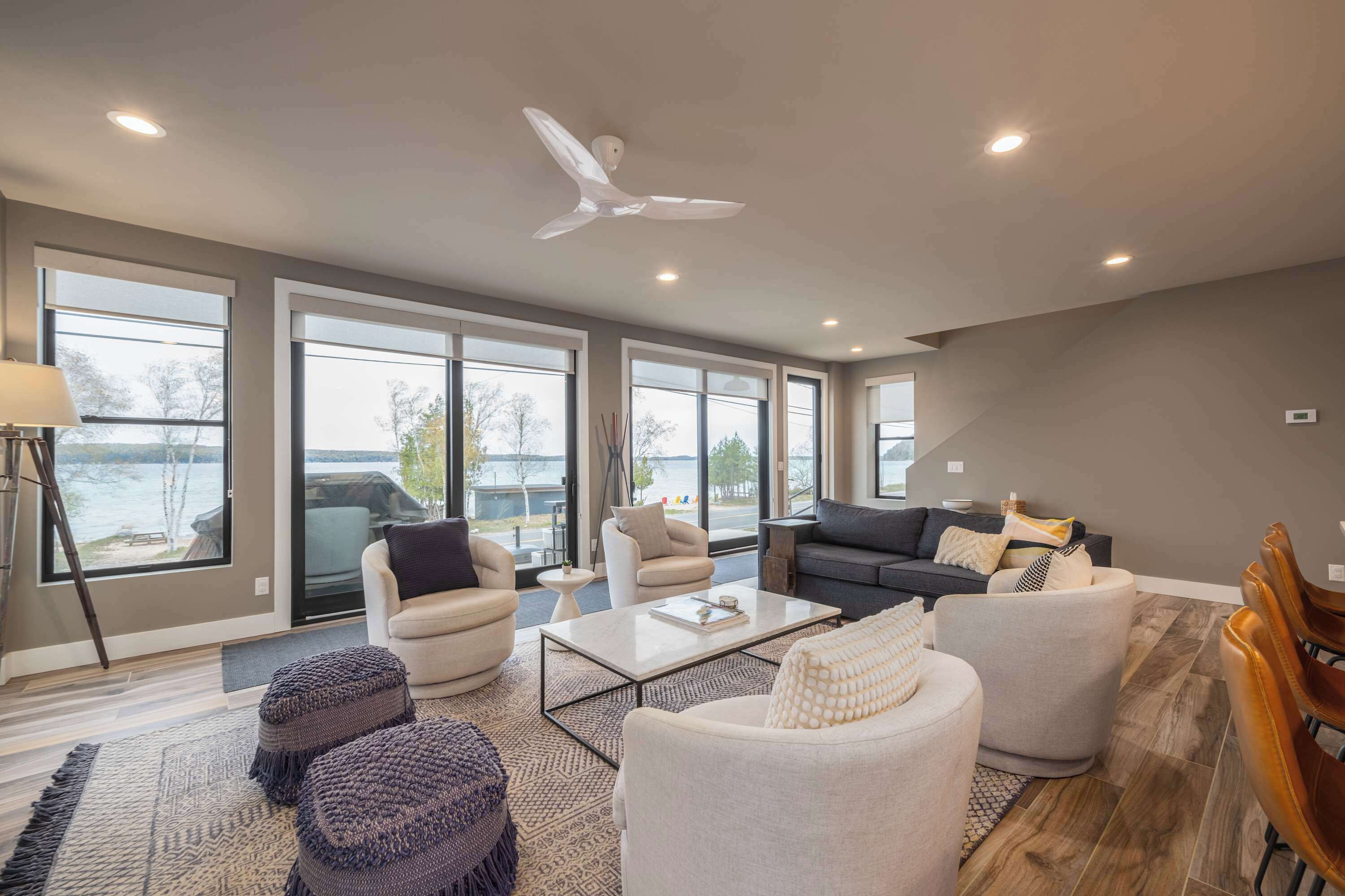 A spacious living room with large windows, a ceiling fan, and a view of the outdoors.