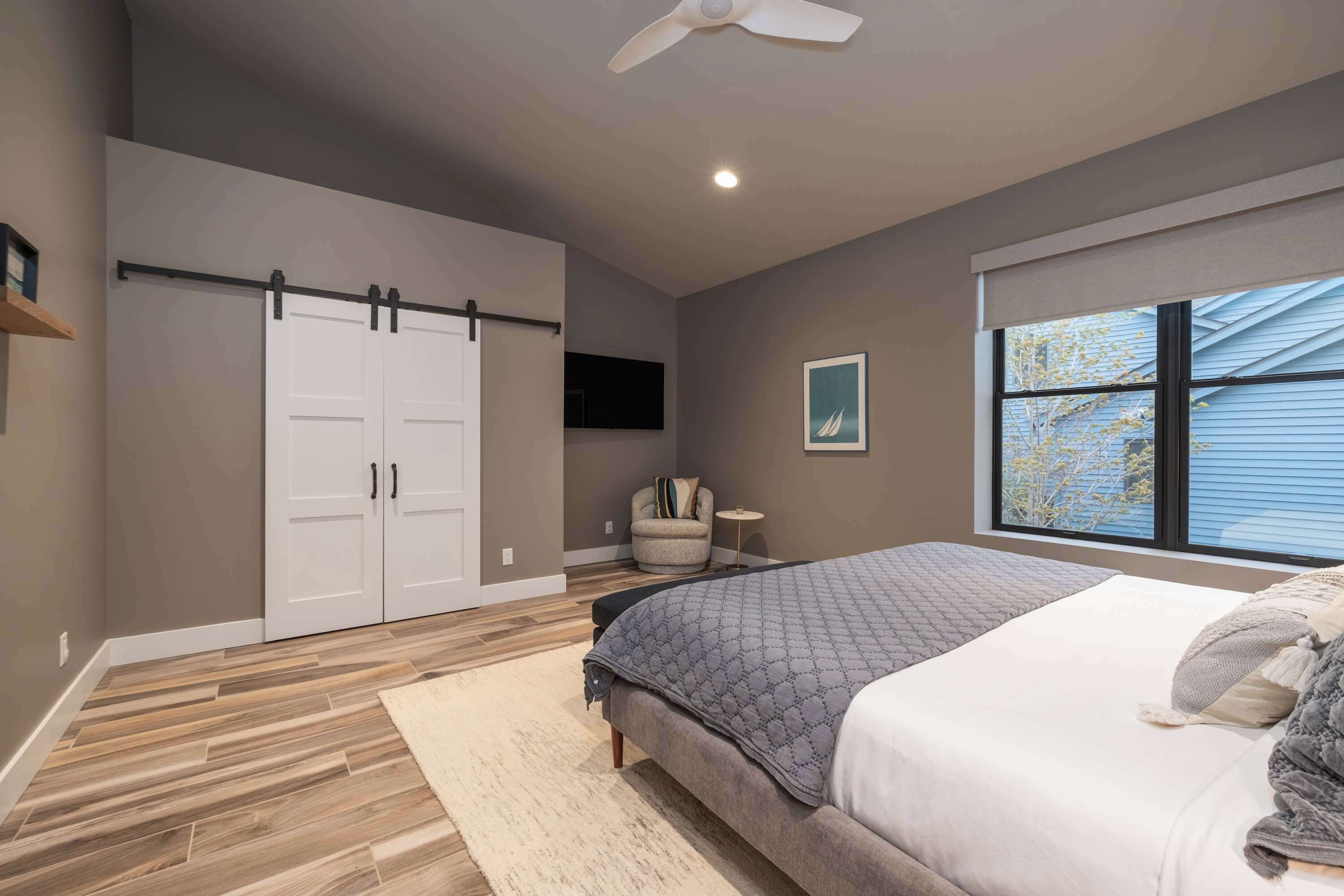 A bedroom with a bed, a ceiling fan, a window, a wardrobe, and a chair.